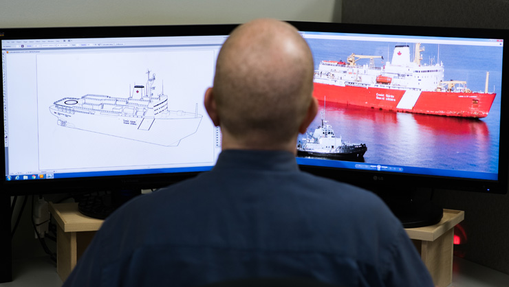 computer monitors showing naval rendering of a ship and the finished ship on the water